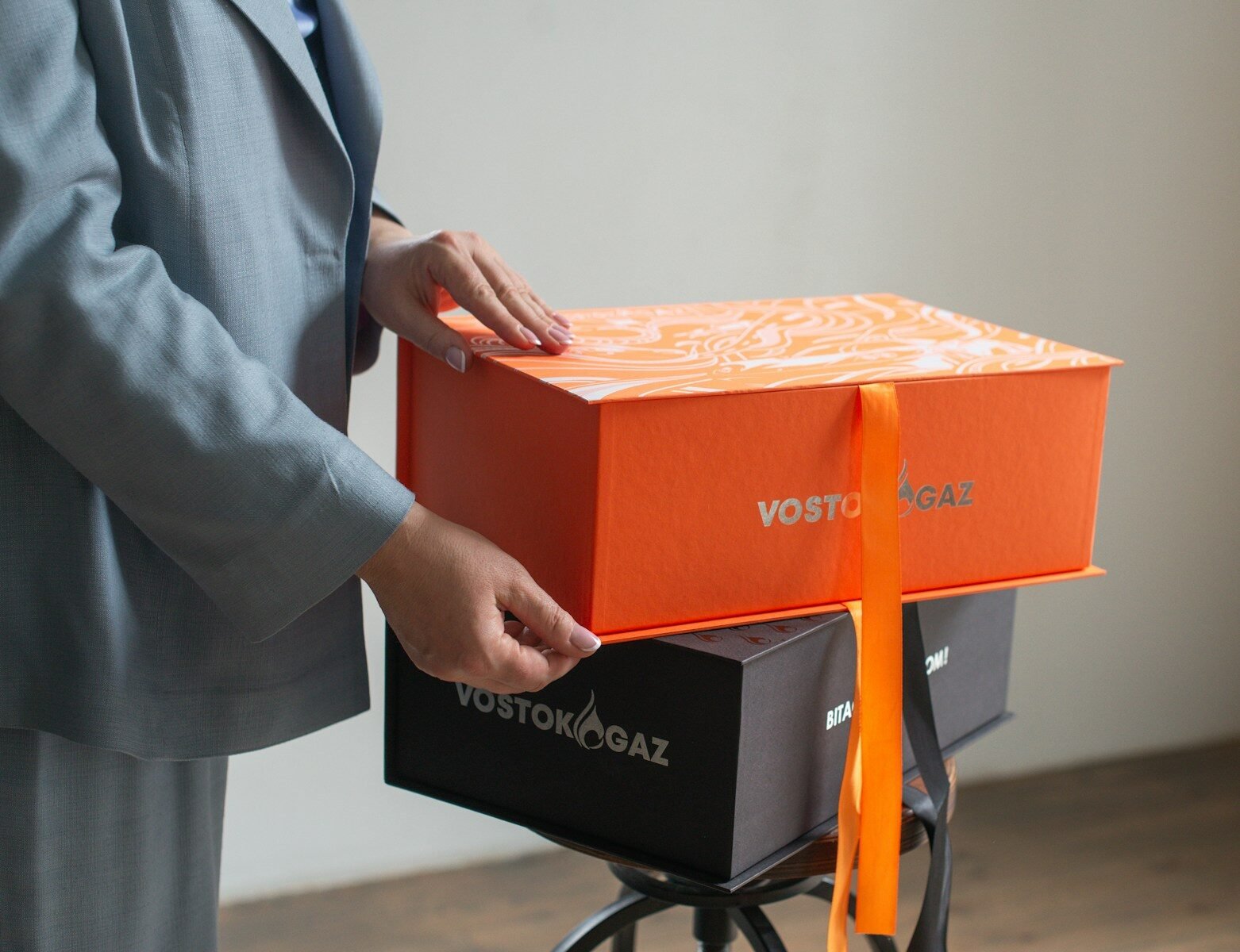 Hands opening a bright orange gift box with ribbon